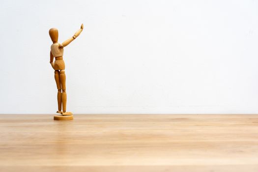 A wooden artist mannequin stands on a wooden table against a plain white background.