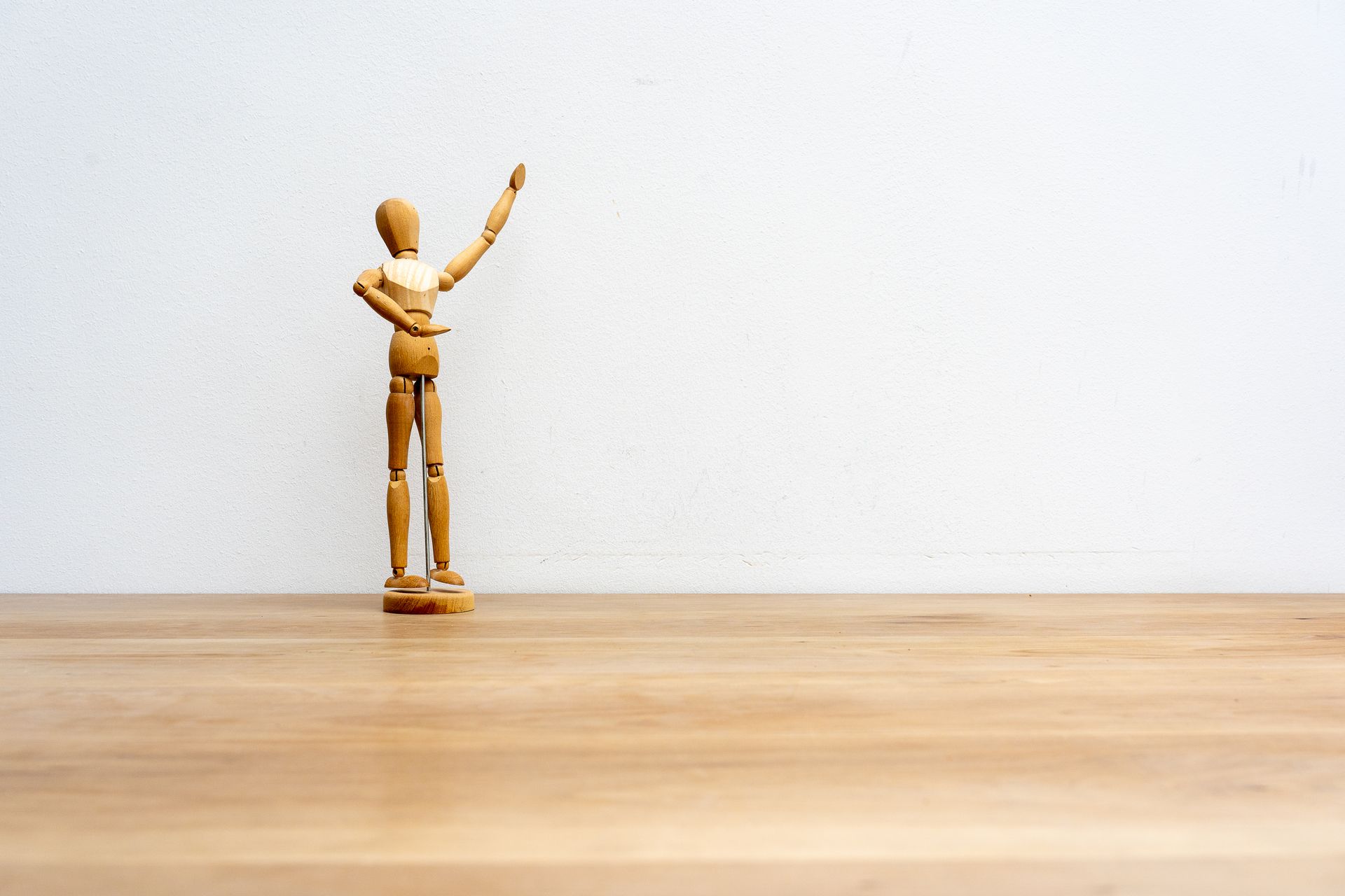 Minimalist image of a wooden art mannequin with a raised arm, perfect for artistic and design concepts.