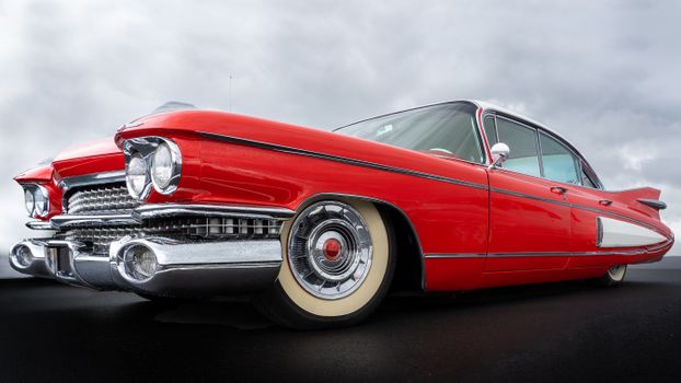 Low-angle view of a vintage red car under an overcast sky highlighting classic design.