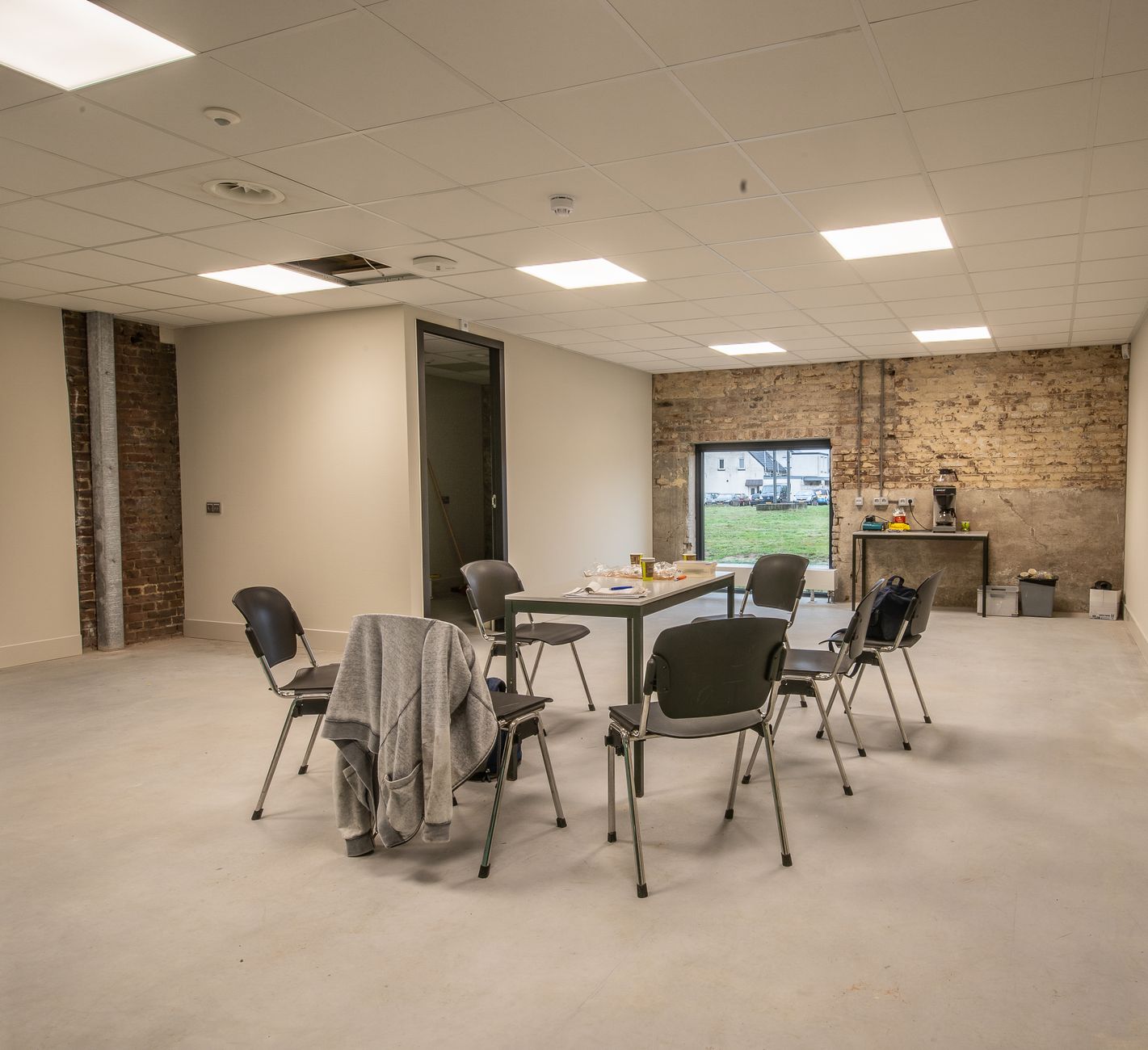 Bright, minimalist meeting room with empty chairs and a table in a modern industrial space.