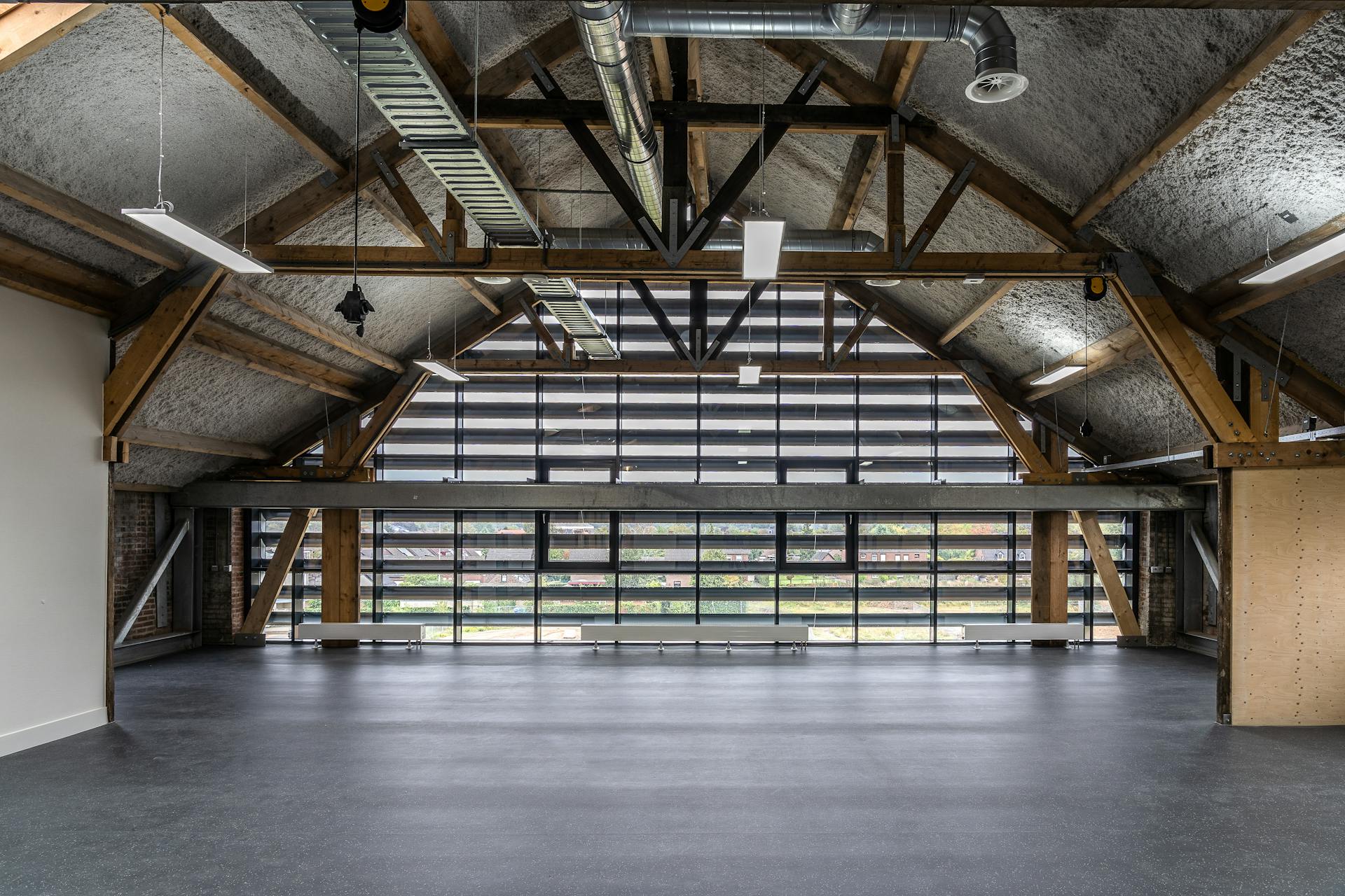 An empty modern industrial hall with timber and steel beams, featuring large windows.