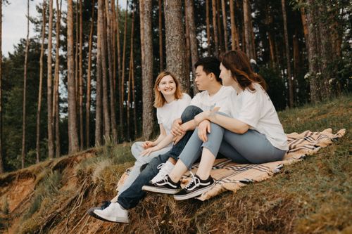 Free A group of friends enjoys a picnic on a blanket in a serene forest setting, sharing smiles and conversation. Stock Photo