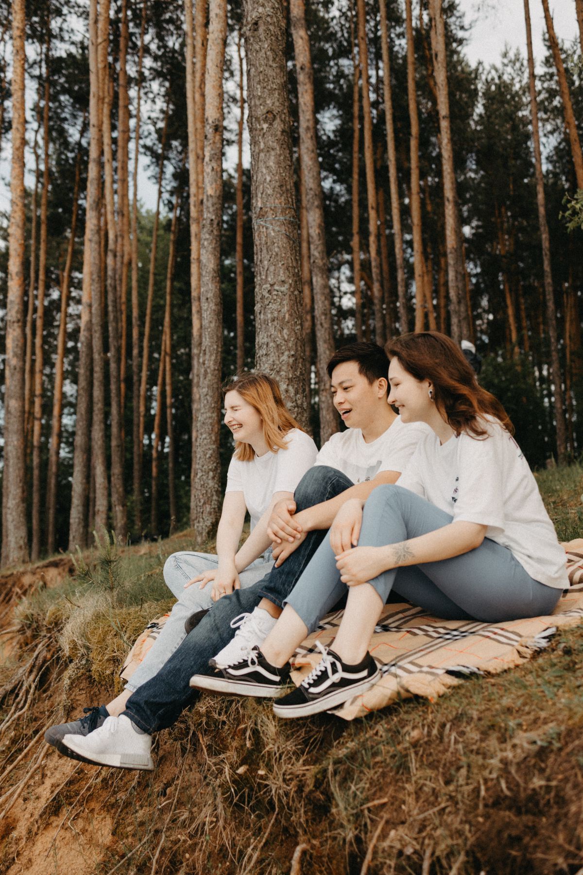 Three friends laughing together on a hillside in a pine forest — photo by Maksim Goncharenok on Pexels