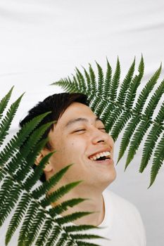 一个男人微笑着，脸上挂着绿色蕨类植物叶子，背景是白色的
