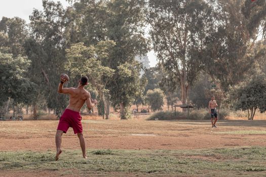 Anonymous shirtless ethnic male athletes training together with soccer ball in green park on sunny day