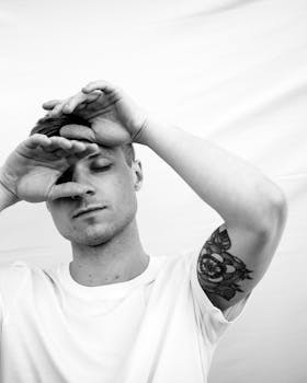 这幅黑白肖像画描绘了一个闭目沉思、双手举起的男人，他身上还有花卉纹身