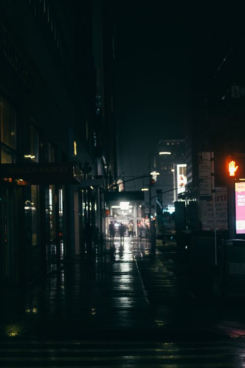Free Back view of unrecognizable people silhouettes strolling on sidewalk between building facades in town with shiny lights at dusk Stock Photo