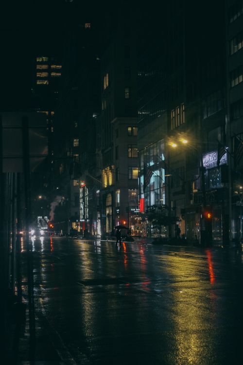 Free Contemporary building exteriors near wet asphalt roadway with vehicle and shiny lights in town at dusk Stock Photo