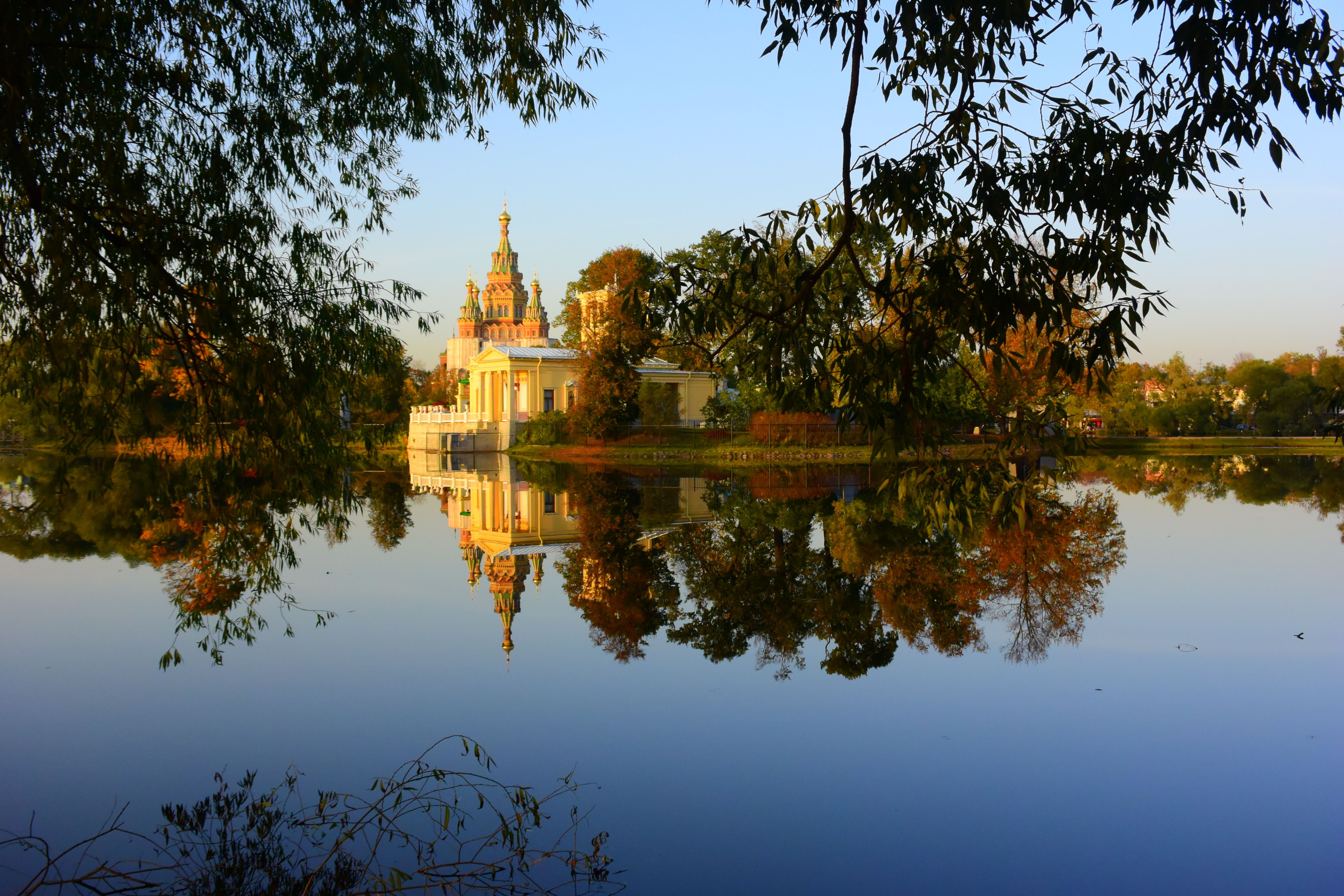 A serene view of Peterhof Palace reflecting in a calm pond in Saint Petersburg during autumn.