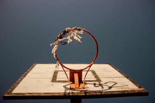 A front view of a weathered basketball hoop against a clear blue sky, symbolizing sport and endurance.