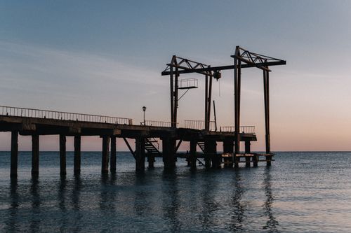 Free Tranquil scene of a rustic pier silhouetted against a dawn sky over calm sea waters. Stock Photo