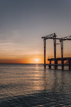 A calming sunset over the sea with a silhouetted pier, perfect for tranquil seaside themes.