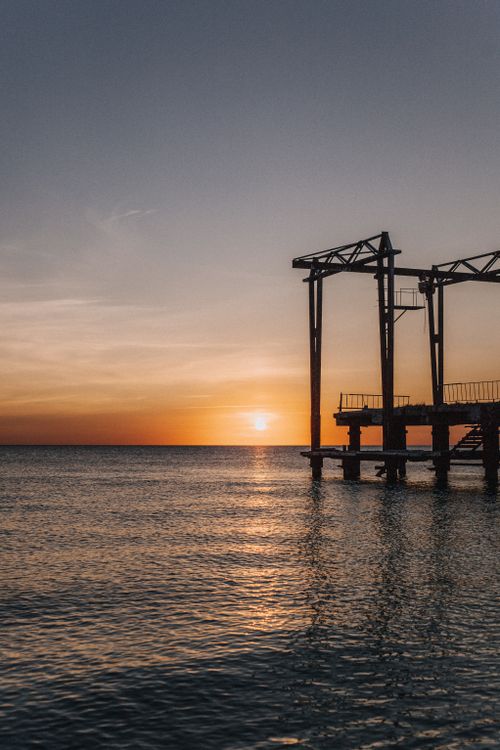Free A calming sunset over the sea with a silhouetted pier, perfect for tranquil seaside themes. Stock Photo
