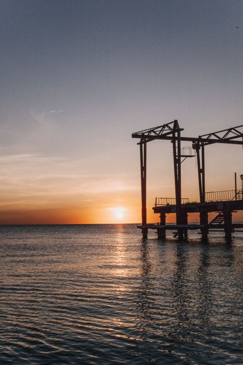 Free A serene view of an offshore platform silhouetted against a vibrant sunset over the sea. Stock Photo
