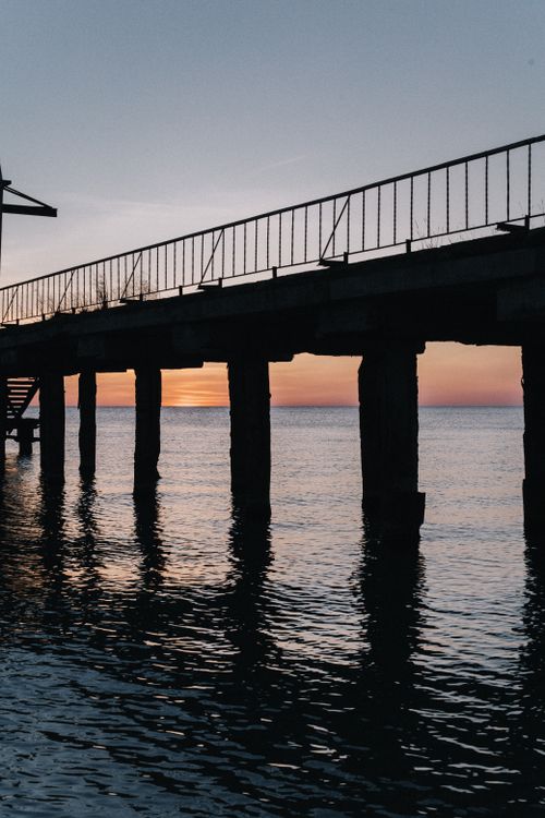 Free A tranquil silhouette view of a pier against a beautiful sunset over calm waters. Stock Photo