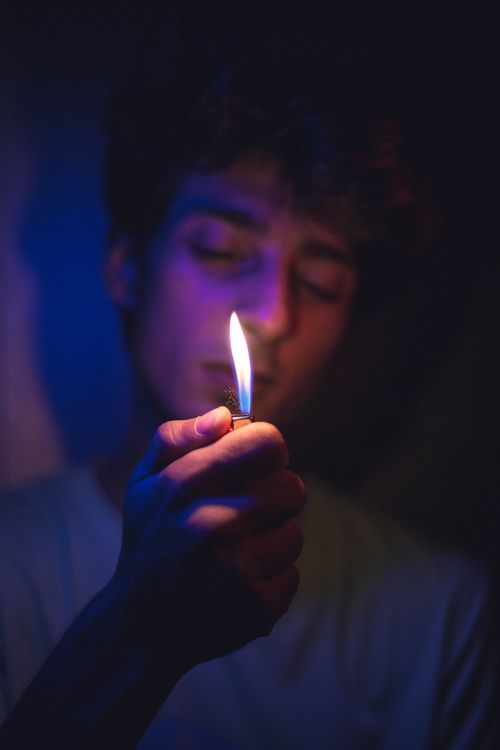 Free A man in dim lighting holds a lighter, creating a vibrant flame with moody tones. Stock Photo
