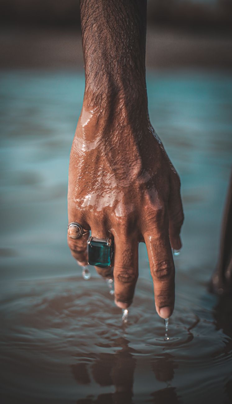 A hand adorned with rings gently touches the surface of water, glistening in natural light.
