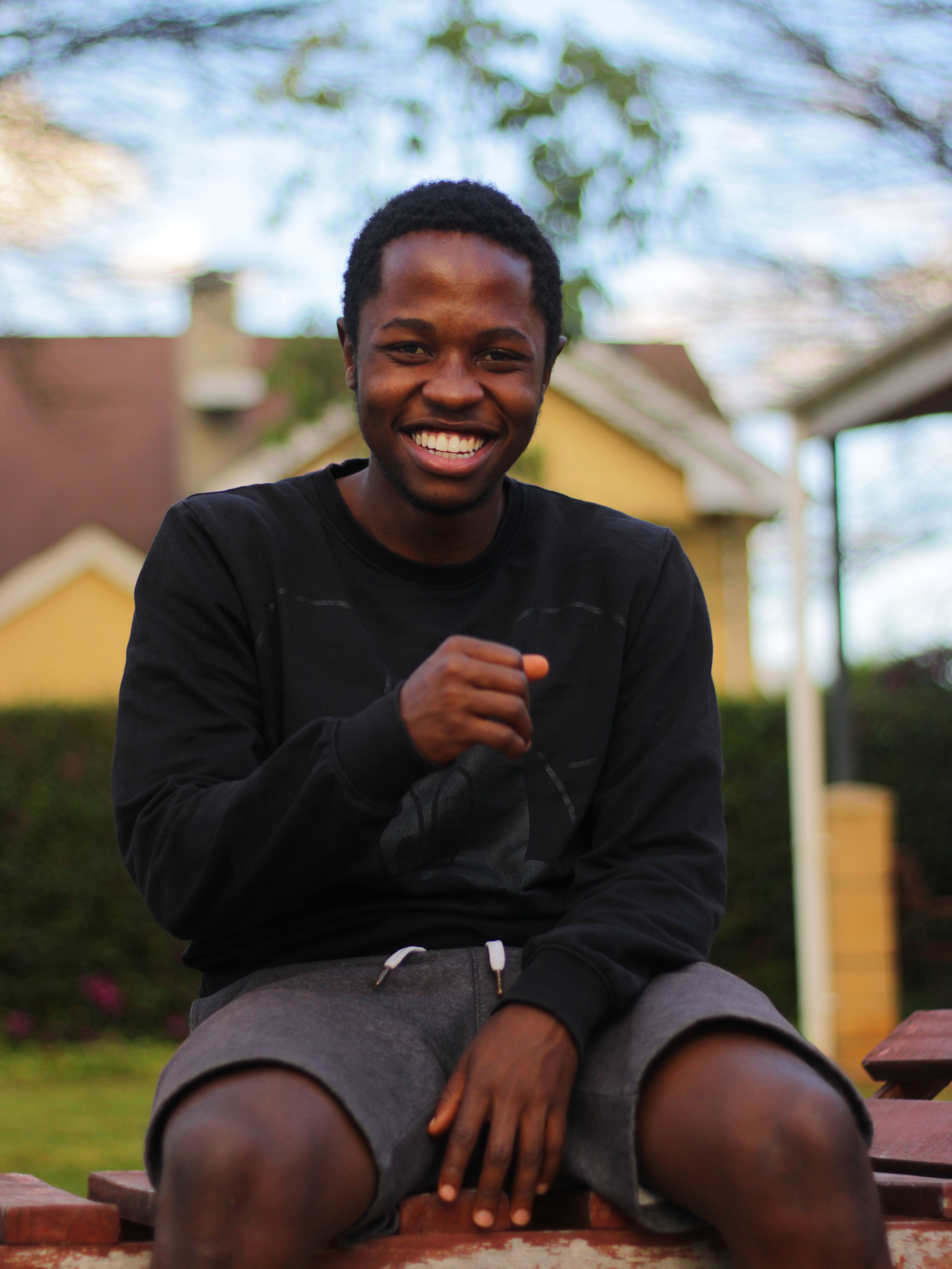 A cheerful man in casual wear smiling while sitting outside in a sunny environment.