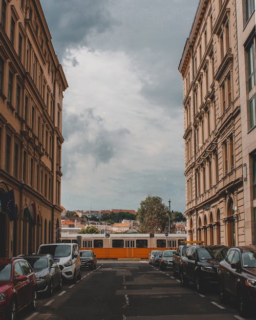 Cars Parked on the Street Between Buildings Under the Cloudy Sky
