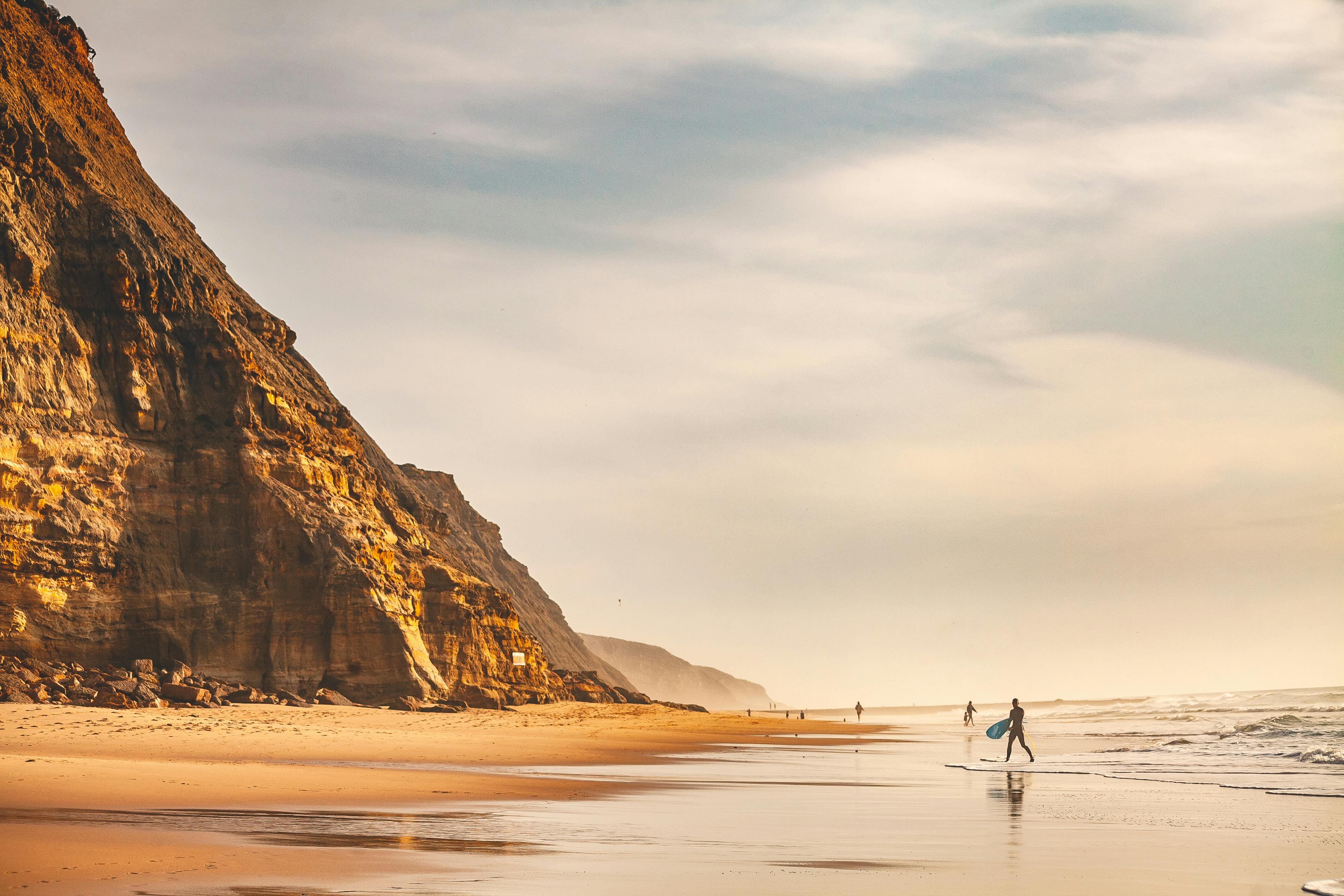 Surfer walking along Ericeira beach with a vibrant sunset and scenic cliffs. Ideal travel destination. - Ericeira