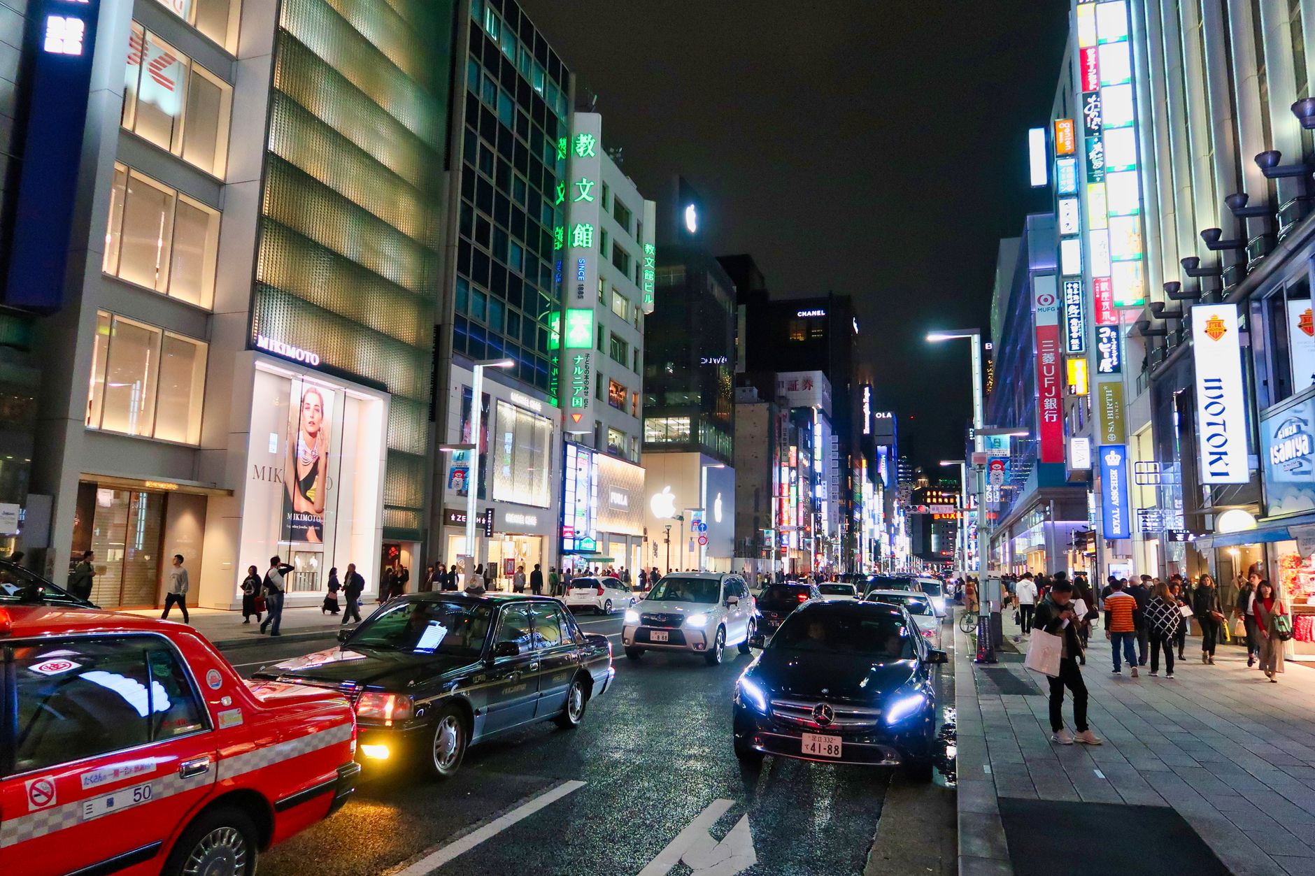Colorful night scene of a busy Tokyo street filled with cars and pedestrians under bright neon lights.