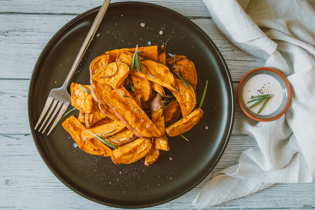 Roasted sweet potato wedges with rosemary on a dark plate with fork and yogurt dip