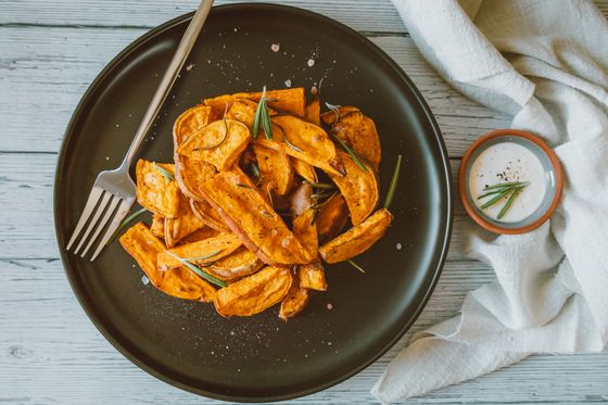 Roasted sweet potato wedges with rosemary on a dark plate with fork and yogurt dip