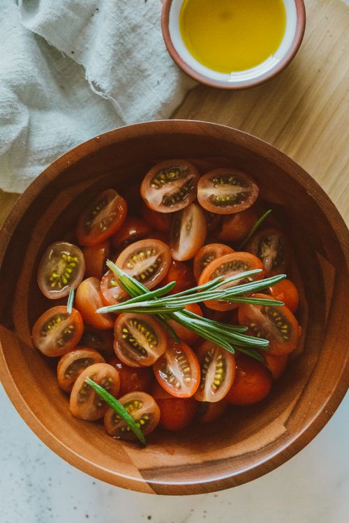 Free Delicious cherry tomato salad with rosemary in a wooden bowl, perfect for a fresh summer meal. Stock Photo