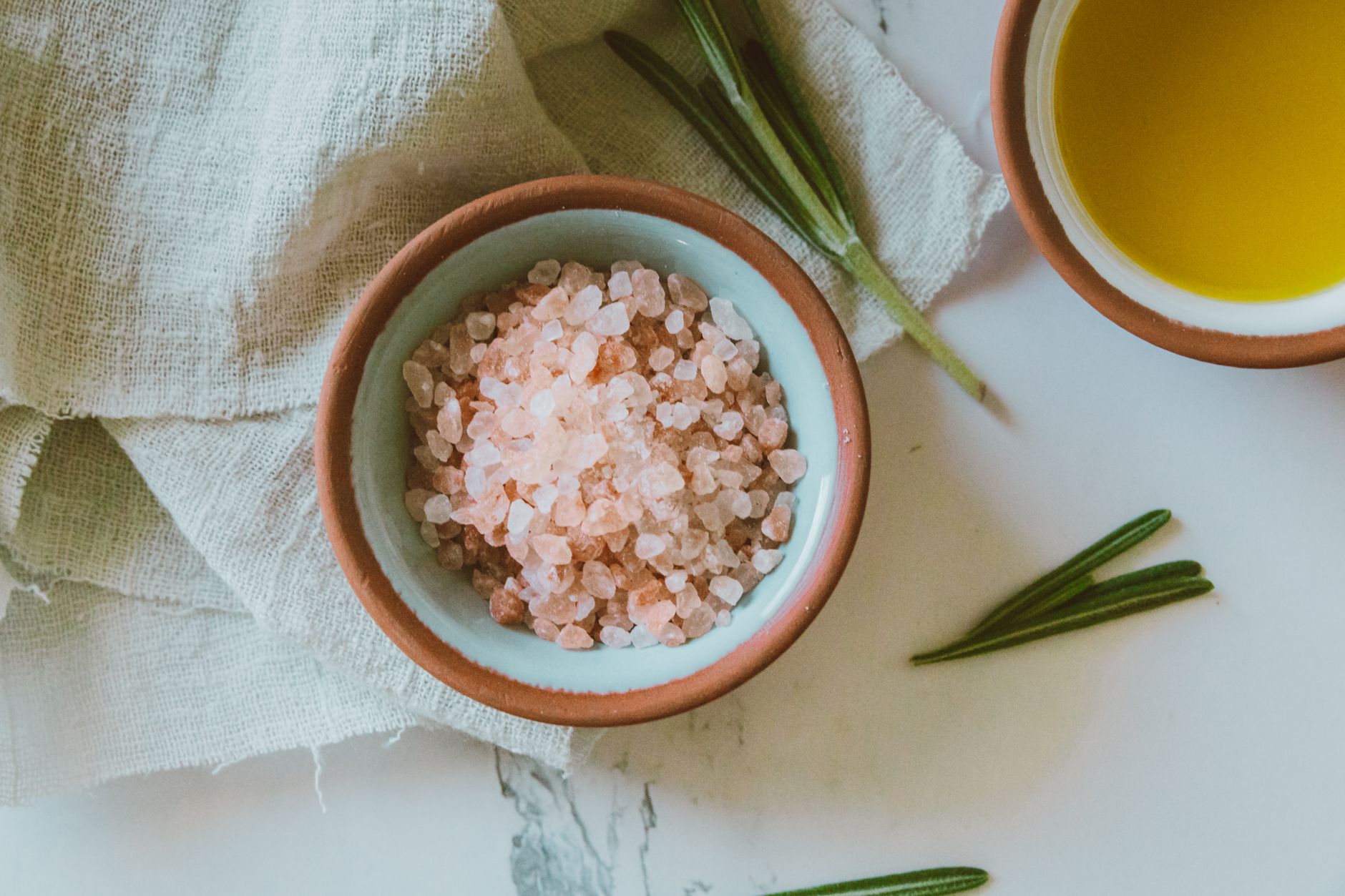 A serene still life featuring pink Himalayan salt in a bowl with olive oil and rosemary, perfect for culinary themes.