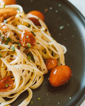 Close-up of a delicious Italian pasta dish with cherry tomatoes and herbs on a black plate.