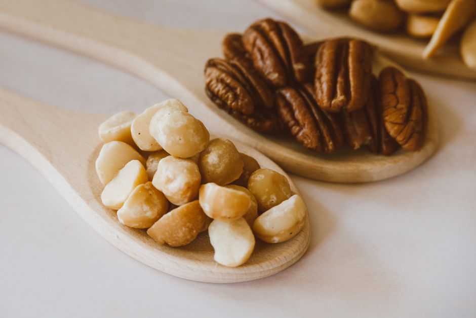 Mẹ Bầu Ăn Hạt Macca Được Không? Nên Ăn Bao Nhiêu Là Tốt Nhất? 4 Detailed photograph showcasing a variety of nuts placed on wooden spoons, emphasizing texture and natural tones.