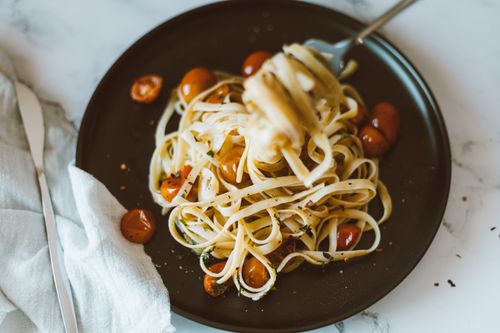 Free Close-up of a delicious Italian pasta dish with cherry tomatoes on a dark plate, garnished with herbs. Stock Photo