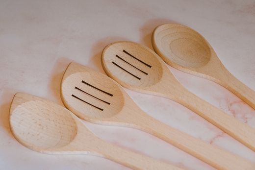 Four light beechwood spoons, two slotted and two solid, on marble