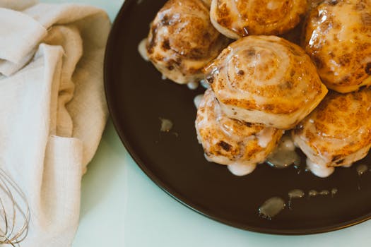 Close-up view of freshly baked cinnamon rolls drizzled with icing on a black plate.