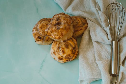 Top view of homemade cinnamon rolls with a whisk on a cloth background, perfect for baking and food themes.