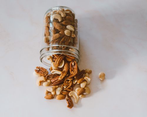 Free Aesthetic image of various nuts spilling from a glass jar onto a light surface. Stock Photo