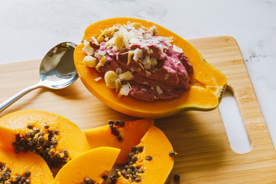 Close-up of sliced papaya topped with berry yogurt and nuts on a wooden board.