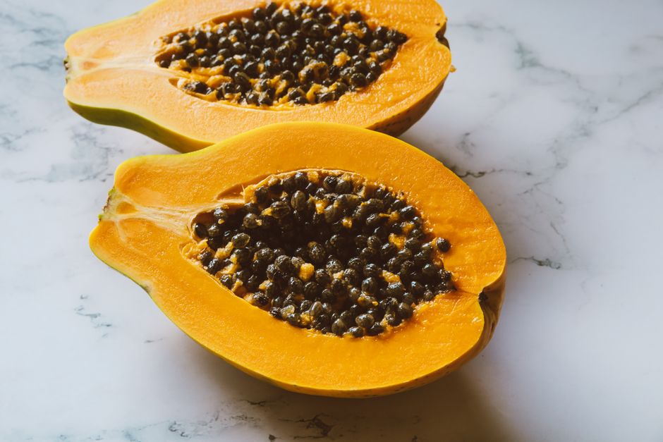 Close-up of freshly sliced papaya halves with seeds on marble background, showcasing vibrant colors.