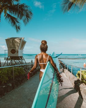 一名女子背着冲浪板，沿着阳光明媚、长满棕榈树的热带海滩小路走过
