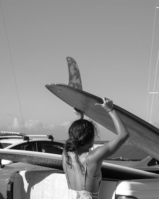 Black and white photo of a woman with a surfboard at the beach.