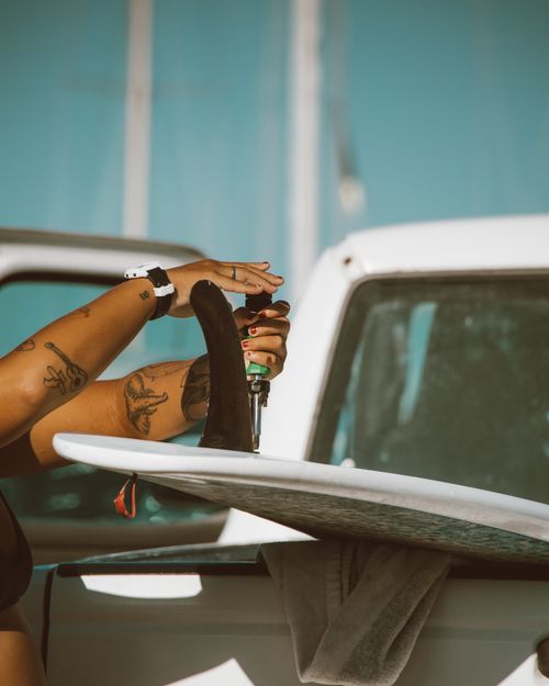 Free A tattooed woman tightens surfboard fins with a screwdriver under summer sunlight. Stock Photo