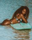 Woman in Pink and White Bikini Lying on Green Surfboard on Body of Water