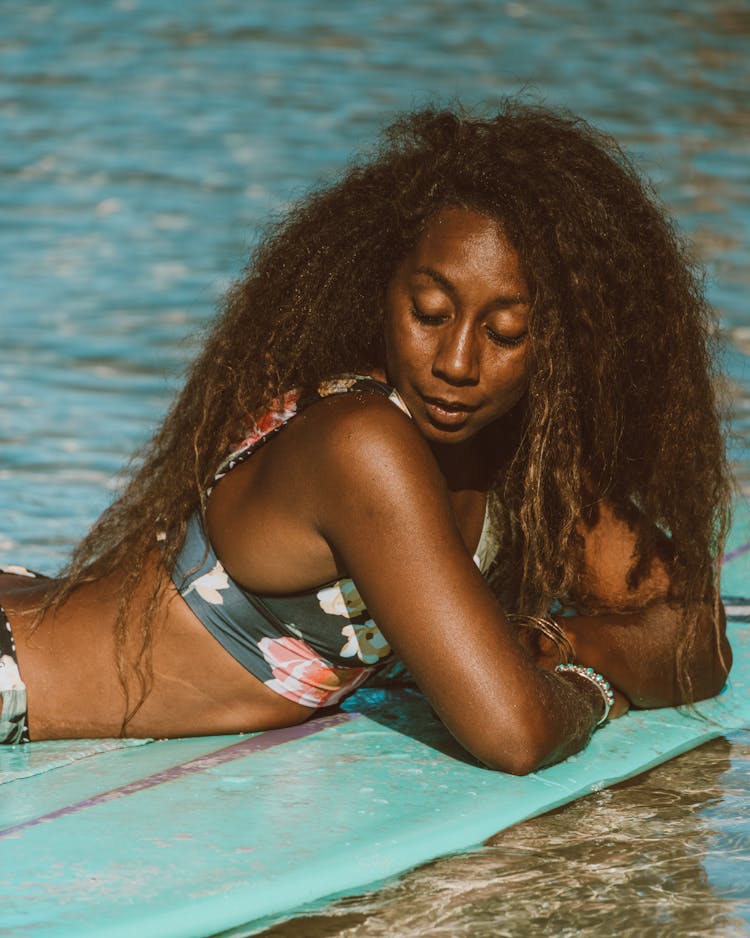 Woman With Afro Hair Resting On Floating Surfboard