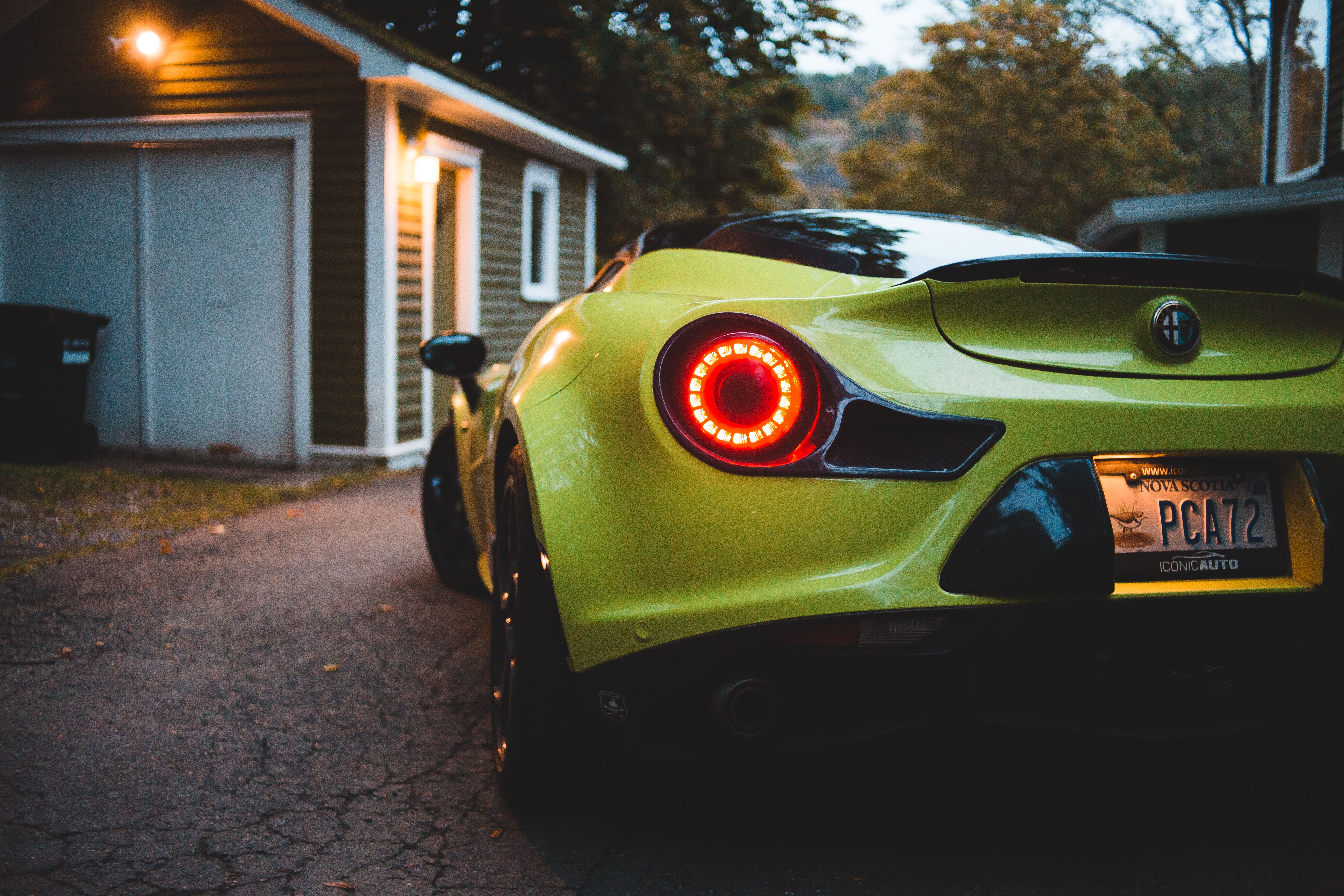 Contemporary luxury racing car with luminous taillight on roadway near small suburban house in evening
