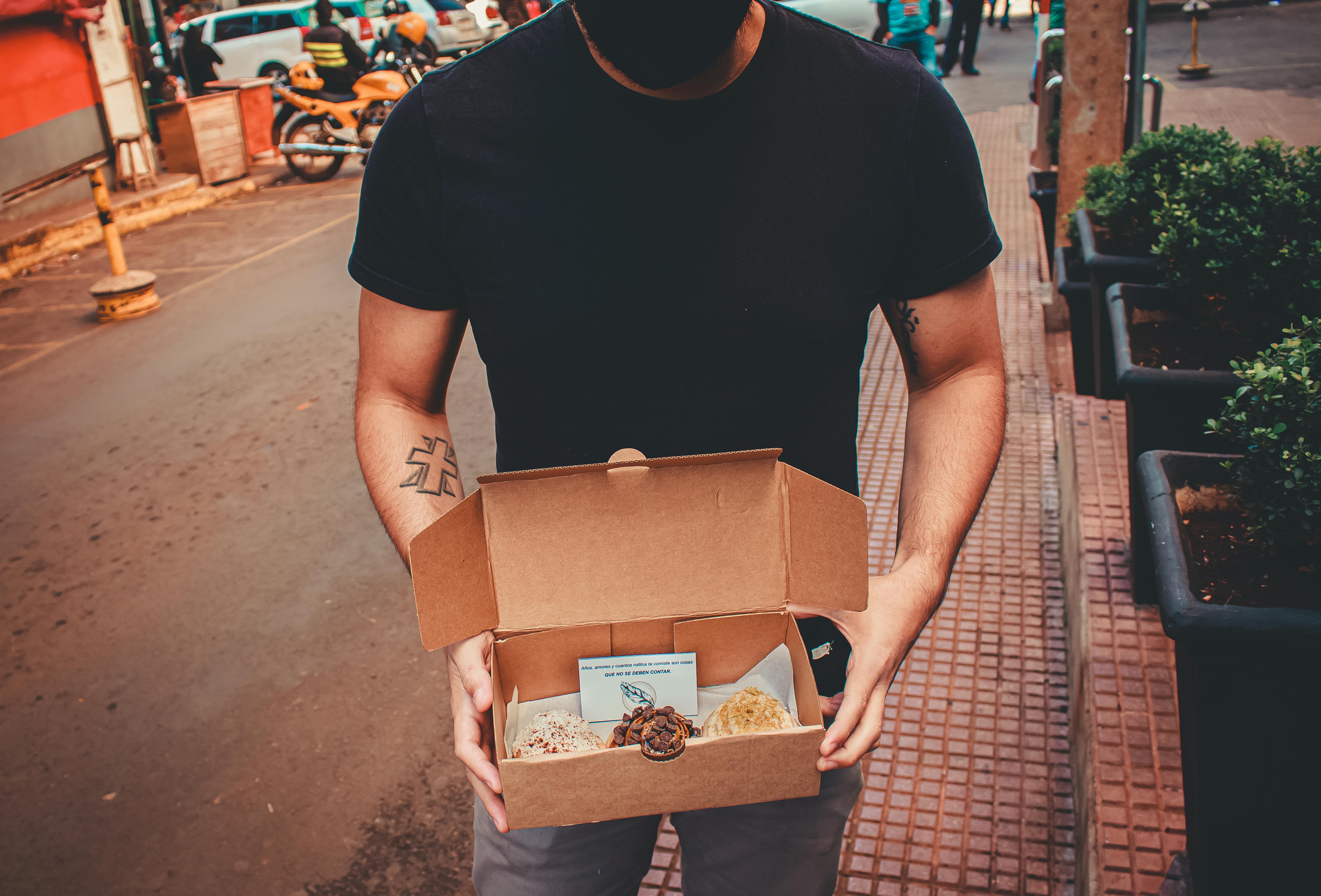 Man holding boxed desserts on a city street. Urban delivery concept.