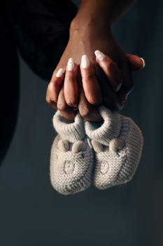 双手轻轻握住针织婴儿鞋的亲密特写，象征着家庭与新生的开始