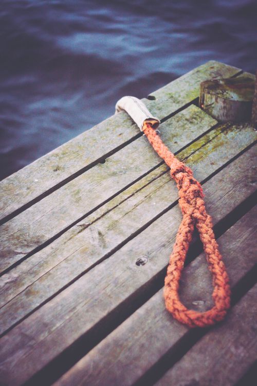 Free Close-up of a rustic wooden dock with a nautical rope by the water. Stock Photo
