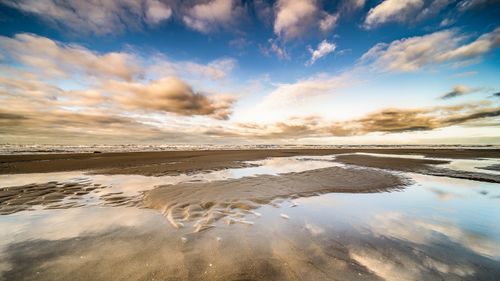 Free A serene beach scene with reflective sand and a vibrant sky showcasing nature's beauty. Stock Photo