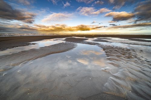 Free Serene beach scene with reflections in tide pools and a vibrant sunset sky. Stock Photo