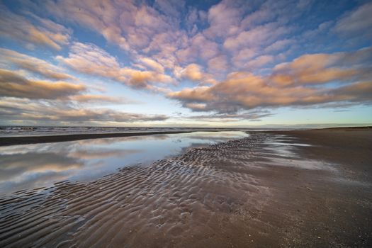 Beautiful beach scene with rippled sand and clouds reflecting the sunrise over the sea.